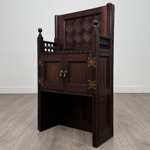 fig 2. A dark mahogany hall seat cabinet featuring a carved geometric back panel, decorative brass strap hinges, double cupboard doors, and finial corner posts.