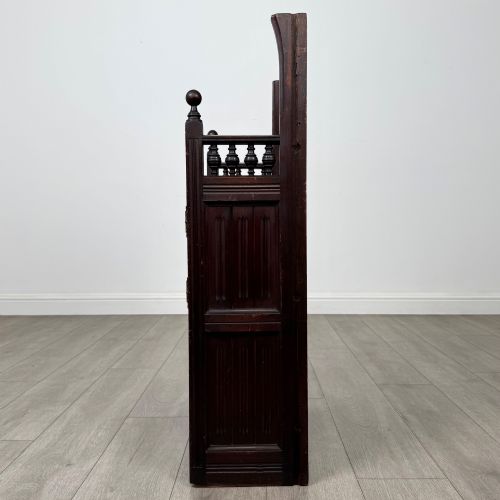 fig 3. A dark mahogany hall seat cabinet featuring a carved geometric back panel, decorative brass strap hinges, double cupboard doors, and finial corner posts.