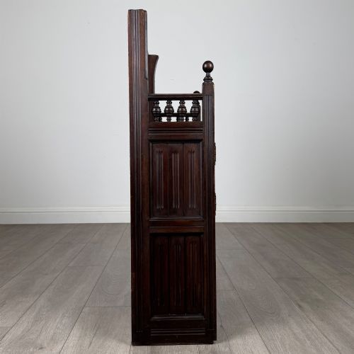 fig 7. A dark mahogany hall seat cabinet featuring a carved geometric back panel, decorative brass strap hinges, double cupboard doors, and finial corner posts.