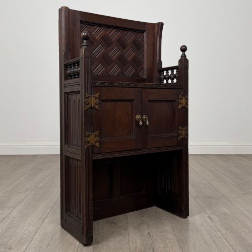 fig 8. A dark mahogany hall seat cabinet featuring a carved geometric back panel, decorative brass strap hinges, double cupboard doors, and finial corner posts.