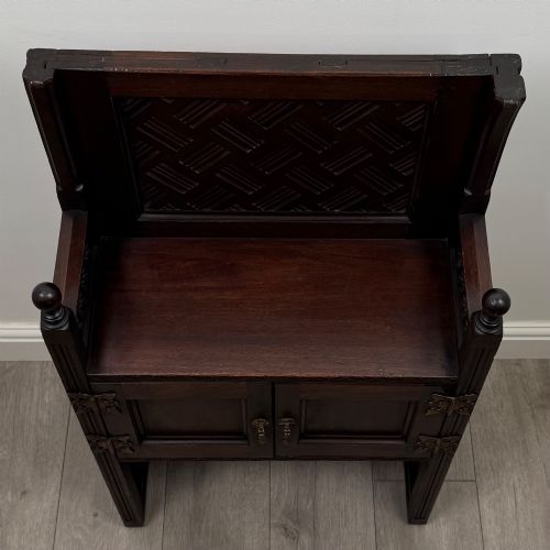 fig 9. A dark mahogany hall seat cabinet featuring a carved geometric back panel, decorative brass strap hinges, double cupboard doors, and finial corner posts.