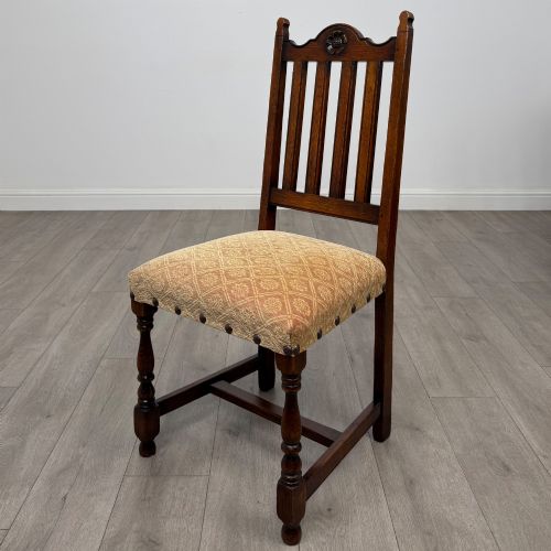 fig 2. A set of six dark oak dining chairs including two armchairs and four side chairs, featuring slat backs with carved crest details and patterned fabric seats.
