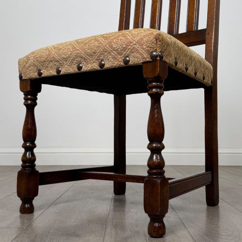 fig 5. A set of six dark oak dining chairs including two armchairs and four side chairs, featuring slat backs with carved crest details and patterned fabric seats.