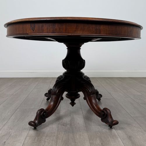 fig 1. A 19th-century Victorian circular rosewood breakfast table with a carved central pedestal column and four scroll legs with brass castors.