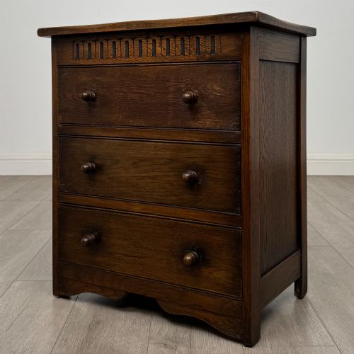 fig 1. A small early twentieth-century dark oak chest of drawers featuring three drawers with turned wooden knobs and a carved frieze top detail.