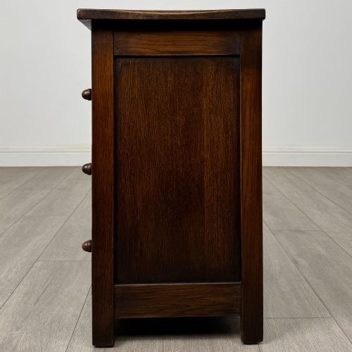 fig 2. A small early twentieth-century dark oak chest of drawers featuring three drawers with turned wooden knobs and a carved frieze top detail.