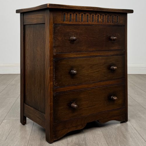 fig 7. A small early twentieth-century dark oak chest of drawers featuring three drawers with turned wooden knobs and a carved frieze top detail.