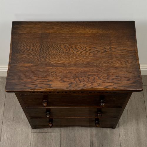 fig 8. A small early twentieth-century dark oak chest of drawers featuring three drawers with turned wooden knobs and a carved frieze top detail.