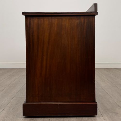 fig 2. An antique Edwardian walnut pedestal desk featuring nine drawers with reeded panel details, brass drop handles, and a carved kneehole arch.