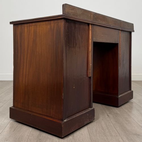 fig 3. An antique Edwardian walnut pedestal desk featuring nine drawers with reeded panel details, brass drop handles, and a carved kneehole arch.