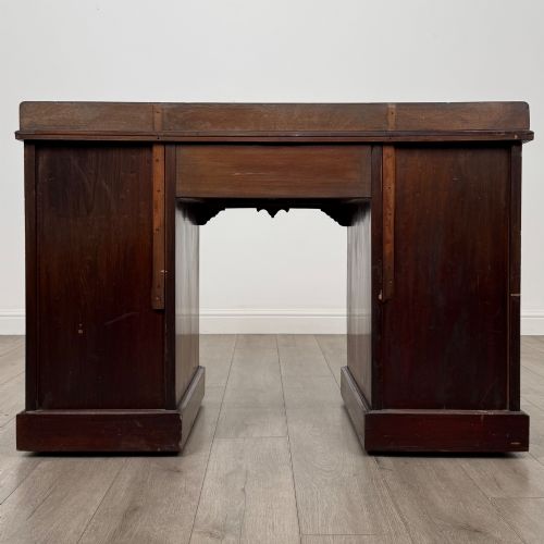fig 4. An antique Edwardian walnut pedestal desk featuring nine drawers with reeded panel details, brass drop handles, and a carved kneehole arch.