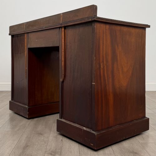 fig 5. An antique Edwardian walnut pedestal desk featuring nine drawers with reeded panel details, brass drop handles, and a carved kneehole arch.