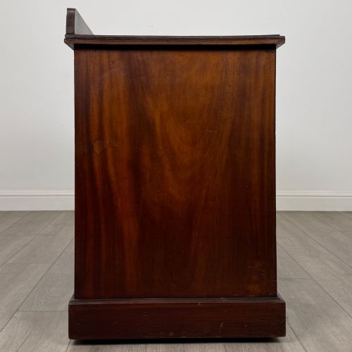 fig 6. An antique Edwardian walnut pedestal desk featuring nine drawers with reeded panel details, brass drop handles, and a carved kneehole arch.