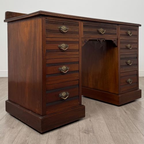 fig 7. An antique Edwardian walnut pedestal desk featuring nine drawers with reeded panel details, brass drop handles, and a carved kneehole arch.
