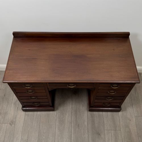 fig 8. An antique Edwardian walnut pedestal desk featuring nine drawers with reeded panel details, brass drop handles, and a carved kneehole arch.