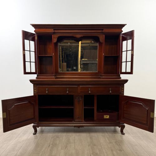 fig 1. An Arts and Crafts dark mahogany sideboard featuring an upper mirrored superstructure flanked by leaded glass cabinet doors above lower drawers and carved cupboards.