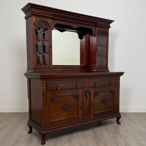 fig 8. An Arts and Crafts dark mahogany sideboard featuring an upper mirrored superstructure flanked by leaded glass cabinet doors above lower drawers and carved cupboards.