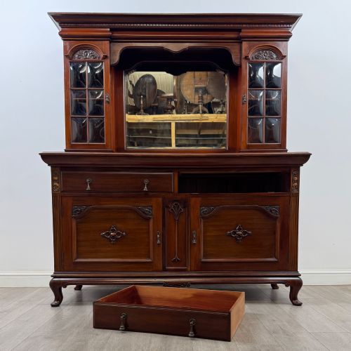 fig 10. An Arts and Crafts dark mahogany sideboard featuring an upper mirrored superstructure flanked by leaded glass cabinet doors above lower drawers and carved cupboards.