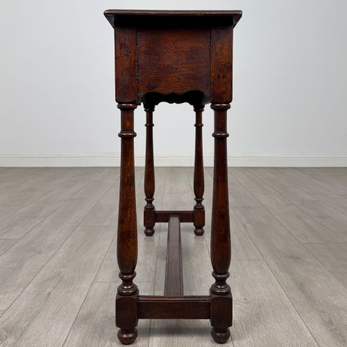 fig 2. A dark oak side table featuring a single wide drawer with brass drop handles, a scalloped apron, turned legs, and lower stretchers.