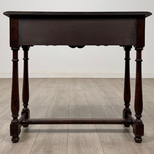 fig 4. A dark oak side table featuring a single wide drawer with brass drop handles, a scalloped apron, turned legs, and lower stretchers.