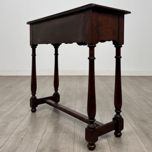 fig 5. A dark oak side table featuring a single wide drawer with brass drop handles, a scalloped apron, turned legs, and lower stretchers.