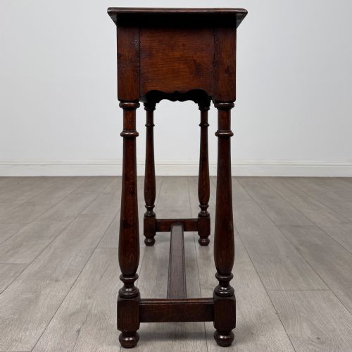 fig 6. A dark oak side table featuring a single wide drawer with brass drop handles, a scalloped apron, turned legs, and lower stretchers.