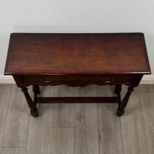 fig 8. A dark oak side table featuring a single wide drawer with brass drop handles, a scalloped apron, turned legs, and lower stretchers.