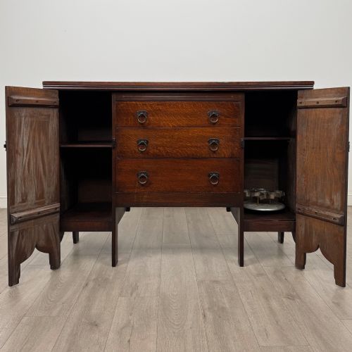 fig 1. A dark oak Gothic Revival sideboard featuring three central drawers with metal drop ring handles, flanked by two carved tracery panel doors with decorative iron latches.