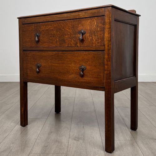 fig 1. A two-drawer golden oak chest of drawers featuring decorative metal drop handles and straight square legs.