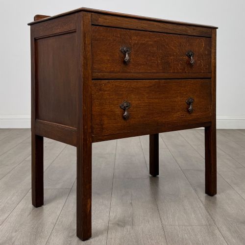 fig 7. A two-drawer golden oak chest of drawers featuring decorative metal drop handles and straight square legs.