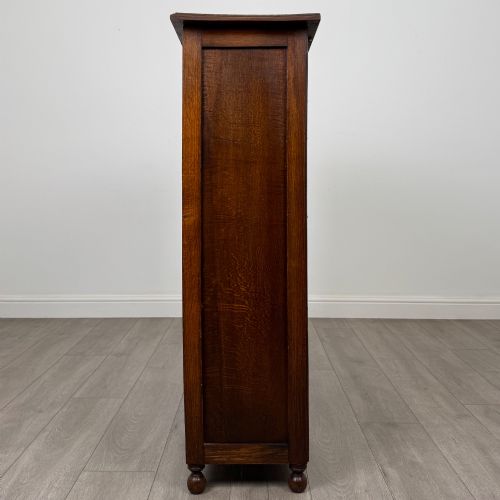 fig 3. An Edwardian warm brown oak display cabinet featuring twin leaded glass doors with a geometric pattern, interior wooden shelves, and rounded bun feet.
