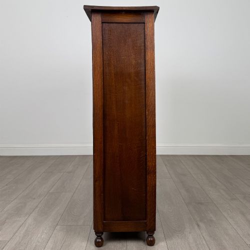 fig 7. An Edwardian warm brown oak display cabinet featuring twin leaded glass doors with a geometric pattern, interior wooden shelves, and rounded bun feet.
