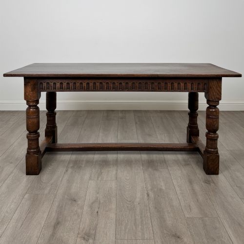 fig 1. A dark oak rectangular refectory dining table featuring a carved arch frieze, four turned legs, and a low H-stretcher.