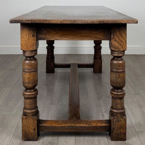 fig 2. A dark oak rectangular refectory dining table featuring a carved arch frieze, four turned legs, and a low H-stretcher.