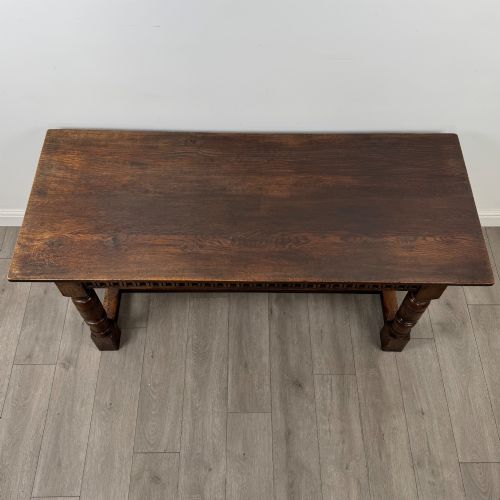 fig 3. A dark oak rectangular refectory dining table featuring a carved arch frieze, four turned legs, and a low H-stretcher.