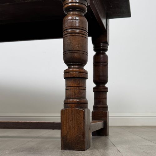 fig 5. A dark oak rectangular refectory dining table featuring a carved arch frieze, four turned legs, and a low H-stretcher.
