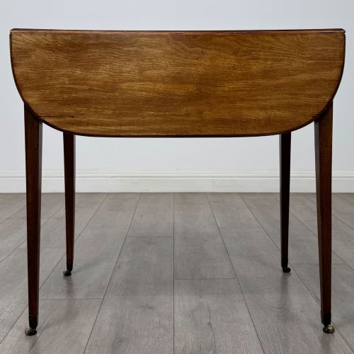 fig 1. A 19th-century Georgian mahogany Pembroke table featuring two hinged drop-leaf sides, a single drawer with wooden knobs, and square tapered legs on brass castors.