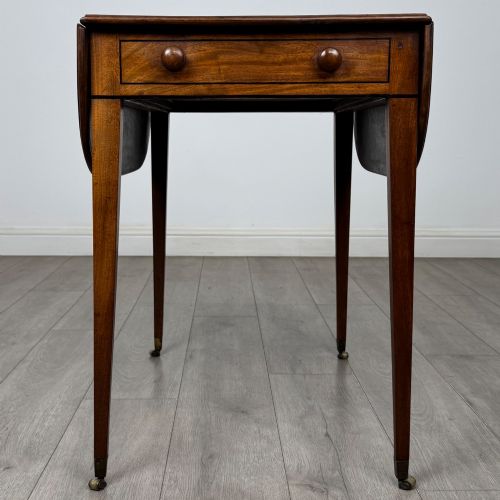 fig 3. A 19th-century Georgian mahogany Pembroke table featuring two hinged drop-leaf sides, a single drawer with wooden knobs, and square tapered legs on brass castors.