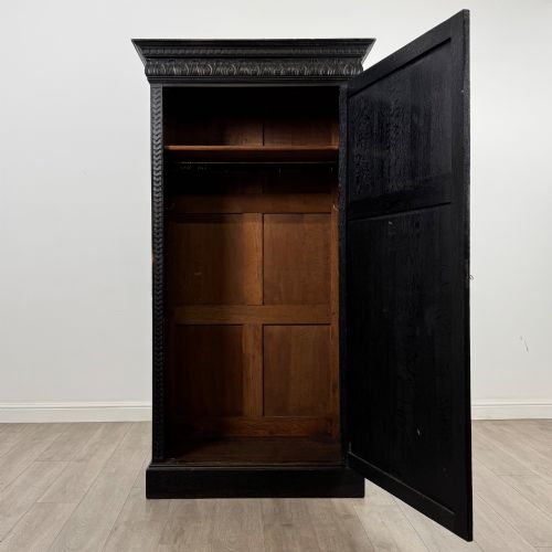 fig 1. A single-door dark oak Victorian wardrobe featuring geometric panel mouldings, a carved relief face in a central diamond, and a pronounced decorative cornice.