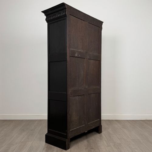 fig 4. A single-door dark oak Victorian wardrobe featuring geometric panel mouldings, a carved relief face in a central diamond, and a pronounced decorative cornice.