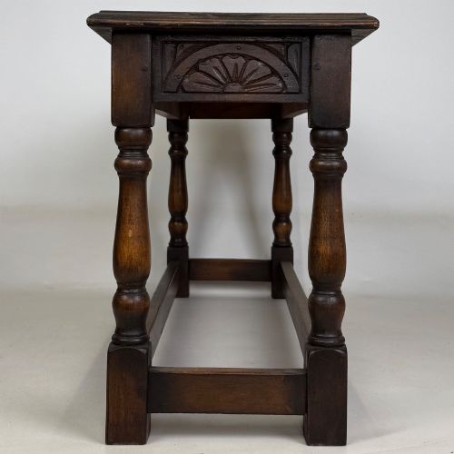 fig 2. A dark carved oak bench featuring turned legs, a lower box stretcher, and a carved lunette frieze along the apron.