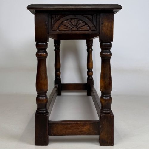 fig 6. A dark carved oak bench featuring turned legs, a lower box stretcher, and a carved lunette frieze along the apron.