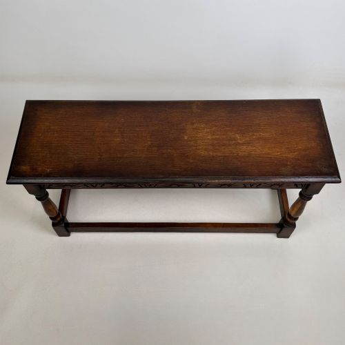 fig 8. A dark carved oak bench featuring turned legs, a lower box stretcher, and a carved lunette frieze along the apron.