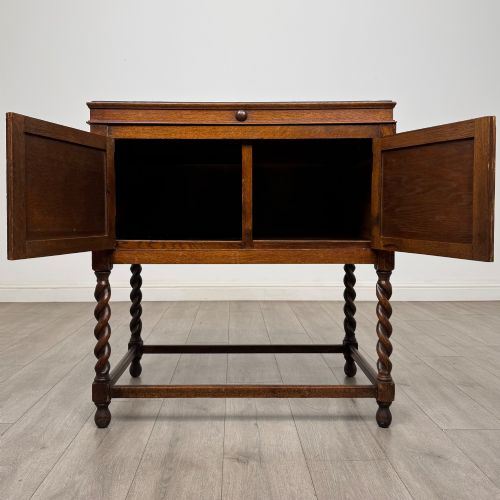 fig 1. A dark oak Jacobean style cabinet featuring two doors with geometric fielded panels, twin brass drop handles, and four barley twist legs supported by low stretchers.