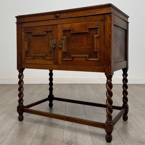 fig 2. A dark oak Jacobean style cabinet featuring two doors with geometric fielded panels, twin brass drop handles, and four barley twist legs supported by low stretchers.