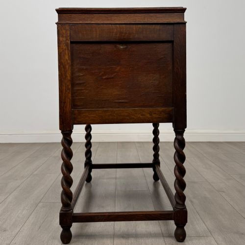 fig 3. A dark oak Jacobean style cabinet featuring two doors with geometric fielded panels, twin brass drop handles, and four barley twist legs supported by low stretchers.