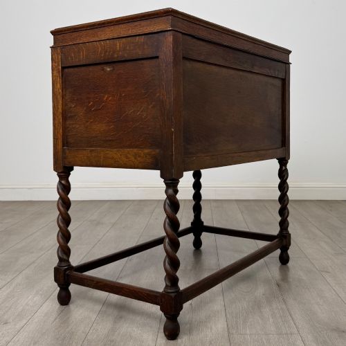 fig 4. A dark oak Jacobean style cabinet featuring two doors with geometric fielded panels, twin brass drop handles, and four barley twist legs supported by low stretchers.