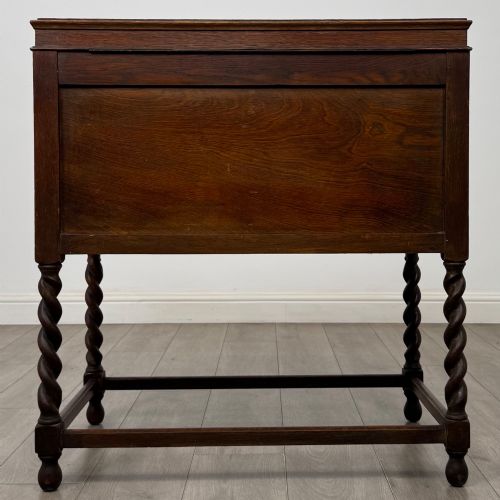 fig 5. A dark oak Jacobean style cabinet featuring two doors with geometric fielded panels, twin brass drop handles, and four barley twist legs supported by low stretchers.
