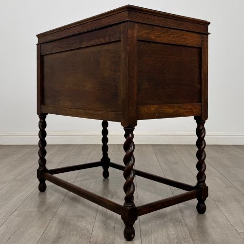 fig 6. A dark oak Jacobean style cabinet featuring two doors with geometric fielded panels, twin brass drop handles, and four barley twist legs supported by low stretchers.