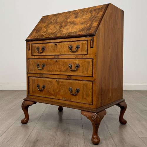 fig 2. An Edwardian burr walnut writing bureau featuring a sloping fall front, three drawers with decorative brass handles, and cabriole legs.